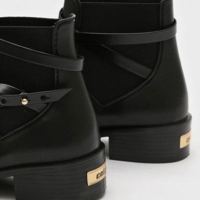 Botins pretos em pele sintética com detalhe de fita e placa dourada na traseira