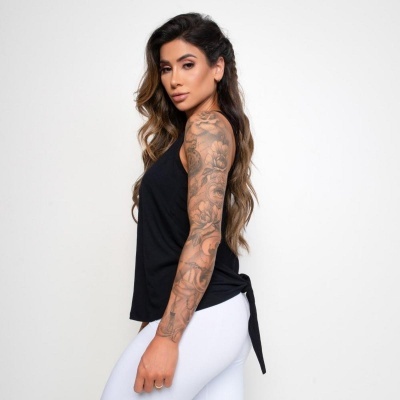 Mulher com camisola preta sem mangas e calças brancas, posando de lado