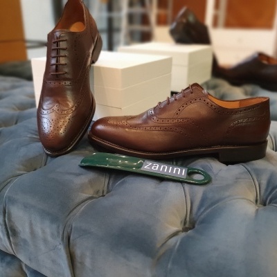 Par de sapatos castanhos de couro com padrão brogue sobre estofado azul com caixas e espátula zanini.