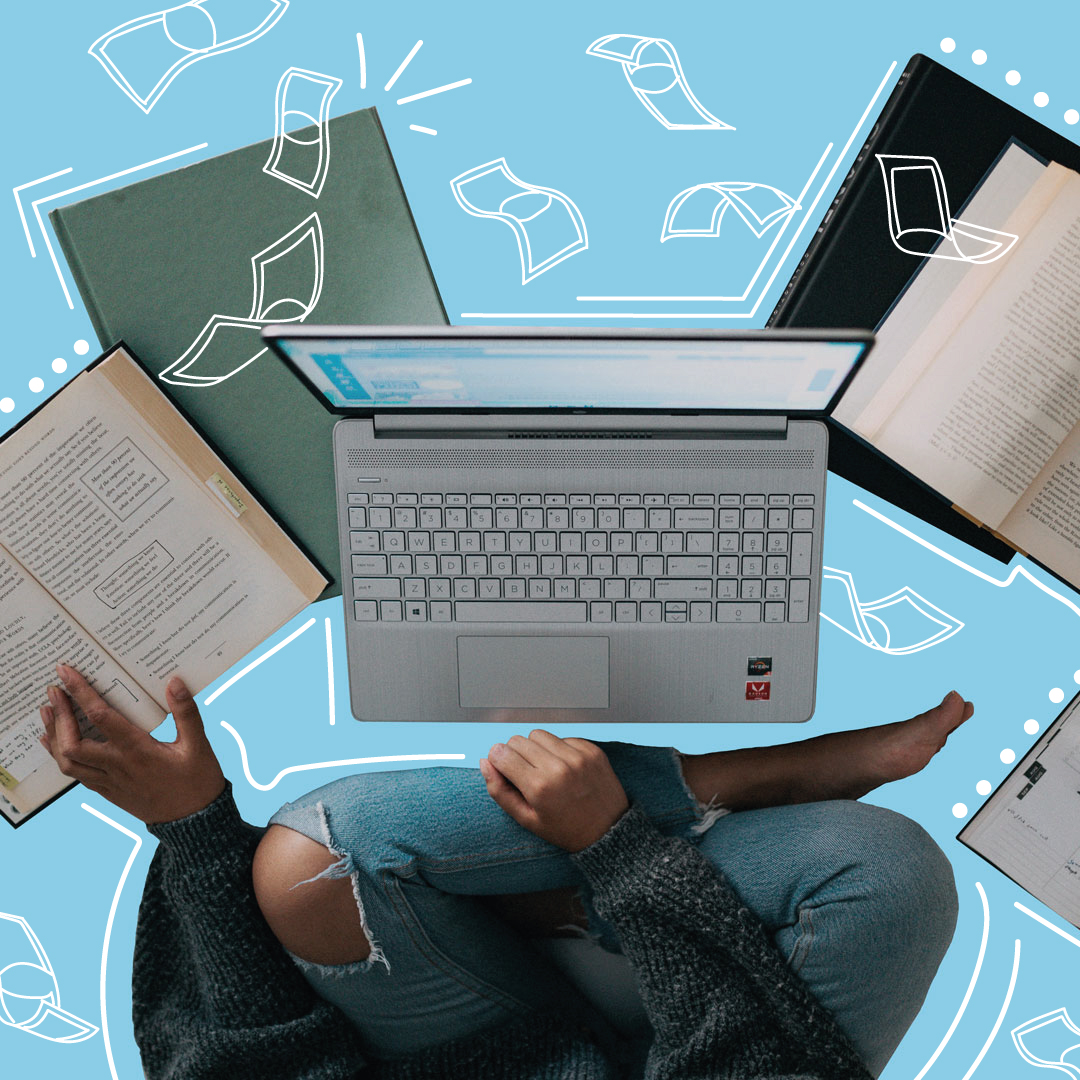 Pessoa sentada de pernas cruzadas com laptop prateado e livros abertos sobre fundo azul claro
