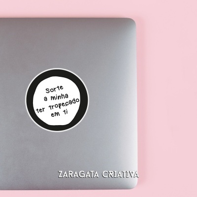 Portátil cinzento com adesivo redondo preto e branco e lápis de madeira clara em fundo rosa