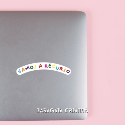 Computador portátil cinza com autocolante colorido e texto branco sobre fundo rosa