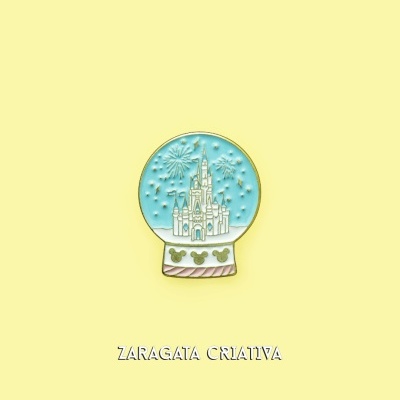 Broche bola de neve com castelo e estrelas, base com padrão e silhuetas Mickey sobre fundo amarelo.