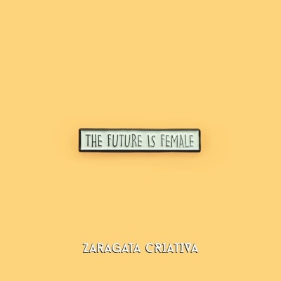 Placa retangular branca com moldura preta e texto THE FUTURE IS FEMALE sobre fundo amarelo, com texto ZARAGATA CRIATIVA em baixo.