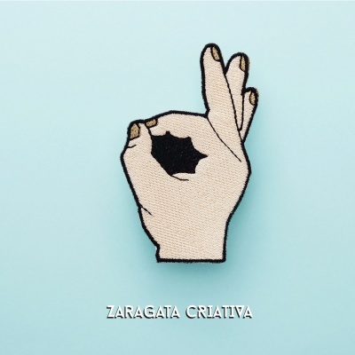 Patch bordado de mão fazendo sinal de ok em fundo azul claro com texto