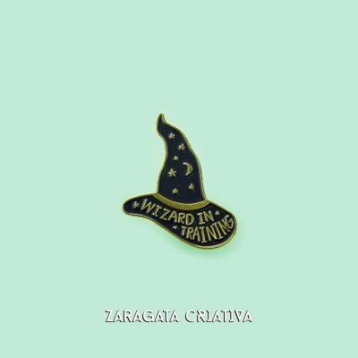 Pin metálico de chapéu de feiticeiro preto com detalhes dourados e texto WIZARD IN TRAINING