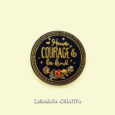Emblema bordado redondo preto e amarelo com texto 'Have COURAGE & be kind' e coração vermelho.
