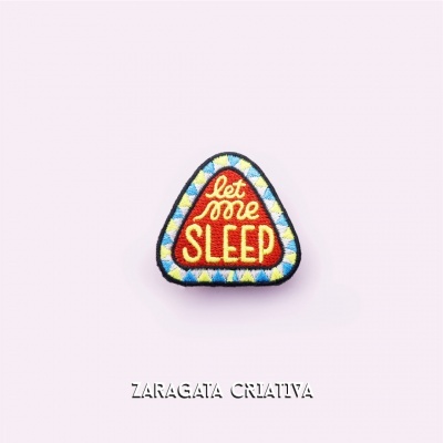 Emblema bordado triangular vermelho com texto 'let me SLEEP' e borda colorida