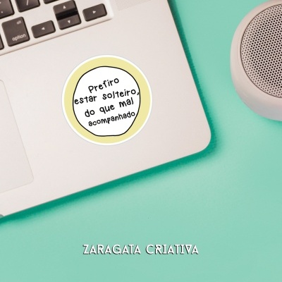 Autocolante com frase num portátil prateado sobre superfície verde-água e coluna de som branca