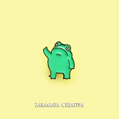 Pin em forma de rã verde com expressão curiosa em fundo amarelo e texto 'ZARAGATA CRIATIVA'