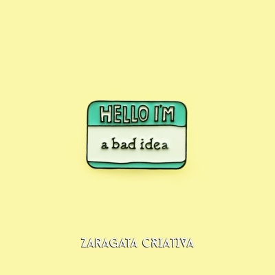 Pin metálico com texto 'HELLO I'M a bad idea' em fundo amarelo