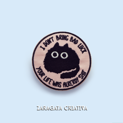 Aplicação bordada redonda com desenho de gato preto e texto em inglês sobre sorte e vida