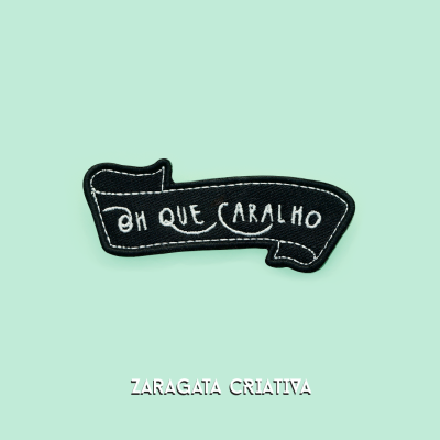 Patch bordado preto com frase 'OH QUE CARALHO' sobre fundo verde claro