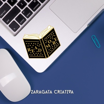 Portátil com autocolante de livro 'READ MORE' e texto 'ZARAGATA CRIATIVA' numa superfície azul