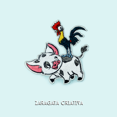 Bordado de porco branco com manchas pretas e galo colorido em fundo azul claro com texto 'ZARAGATA CRIATIVA'