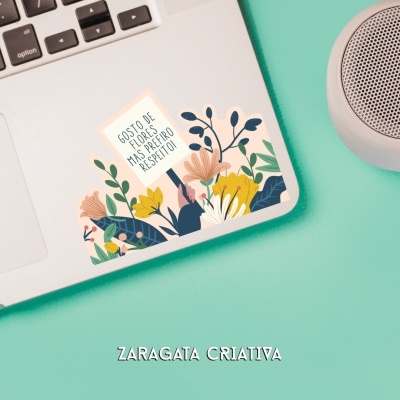 Sticker de flores coloridas com texto em portátil cinza sobre mesa verde ao lado de coluna sonora cinza