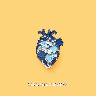 Pin em forma de coração com ondas azuis e brancas sobre fundo amarelo com texto ZARAGATA CRIATIVA