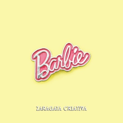 Broche com a palavra Barbie em rosa com contorno dourado sobre fundo amarelo