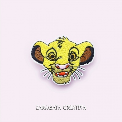 Aplicação bordada da cabeça do Simba em tecido com fundo roxo claro