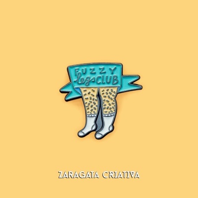 Pin metálico com design de pernas tatuadas e faixa azul com texto FUZZY legs CLUB