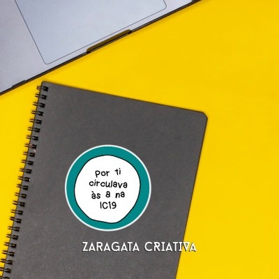 Caderno cinza com autocolante circular com texto POR TI CIRCULAVA ÀS 8 NA IC19 ao lado do portátil