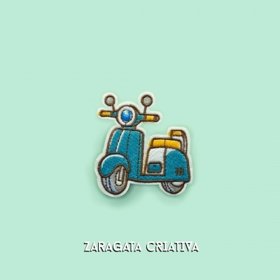 Patch bordado de scooter azul e amarelo em fundo verde-água com texto ZARAGATA CRIATIVA
