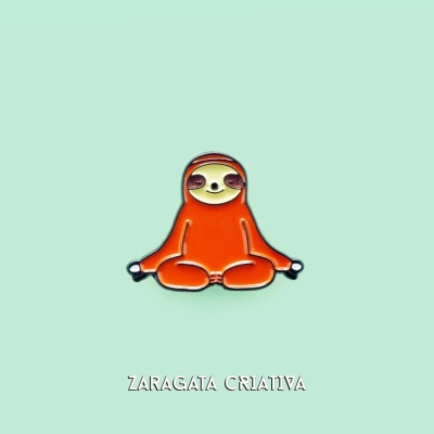 Pin de bicho-preguiça sentado laranja sobre fundo verde água com texto ZARAGATA CRIATIVA