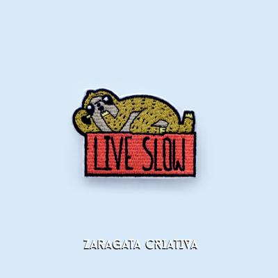 Emblema bordado com bicho preguiça amarelo e texto LIVE SLOW em retângulo coral