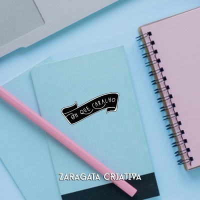 Cadernos azuis claros com autocolante e caneta rosa numa mesa azul clara