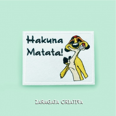 Etiqueta branca bordada com personagem Timão e texto Hakuna Matata