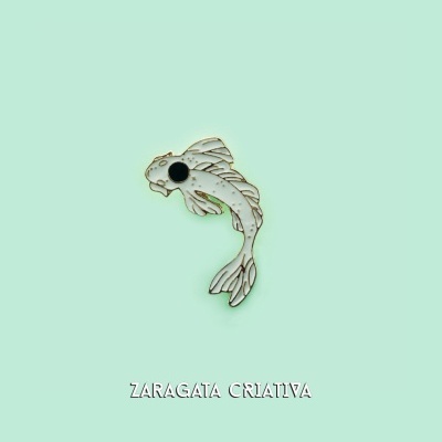 Broche em forma de peixe prateado com olhos pretos sobre fundo verde claro com texto