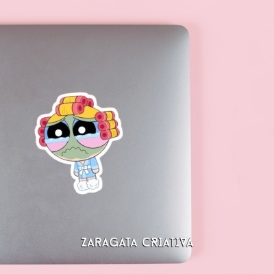 Computador portátil prateado com autocolante de personagem animado e lápis em fundo rosa