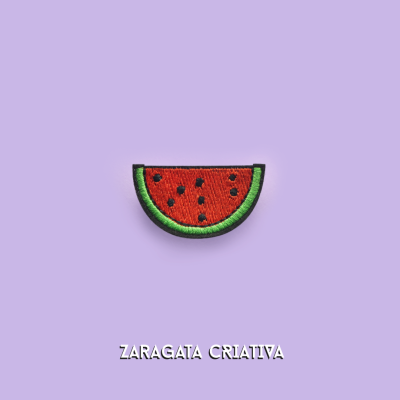 Emblema bordado de fatia de melancia sobre fundo lilás com texto ZARAGATA CRIATIVA