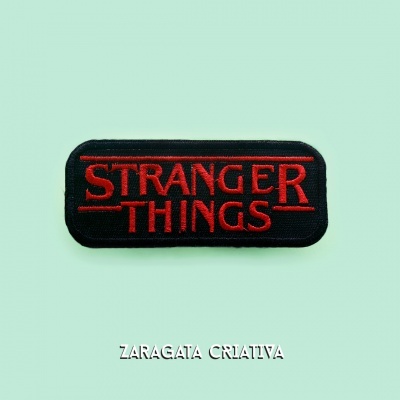 Patch preto e vermelho com texto Stranger Things sobre fundo verde claro