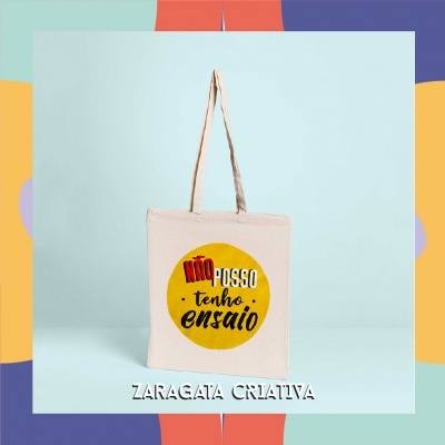 Saco de tecido bege com texto em círculo amarelo e fundo azul claro.