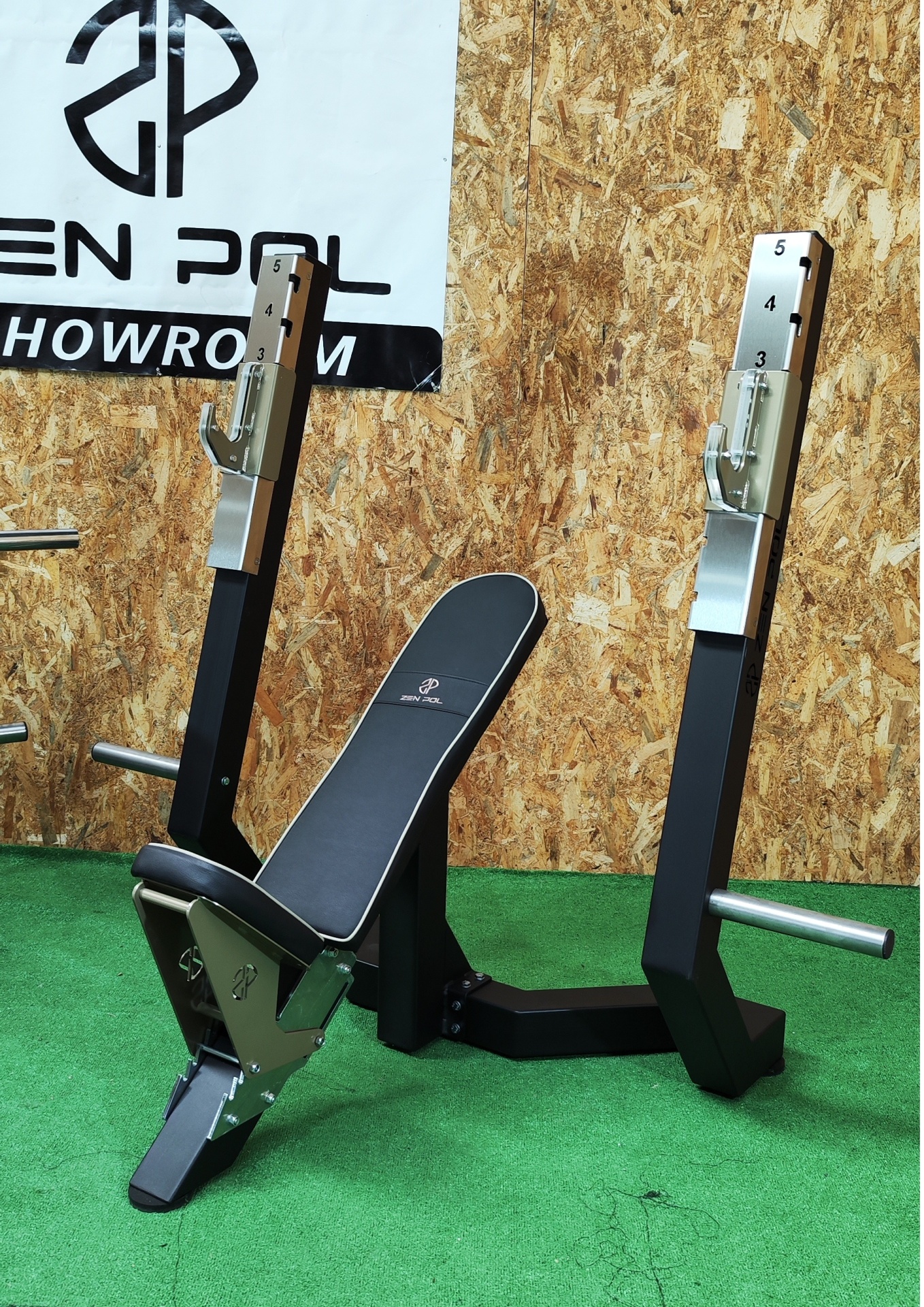 Banco de musculação preto com estrutura metálica e logótipo 'OPEN POL SHOWROOM' em fundo de madeira.