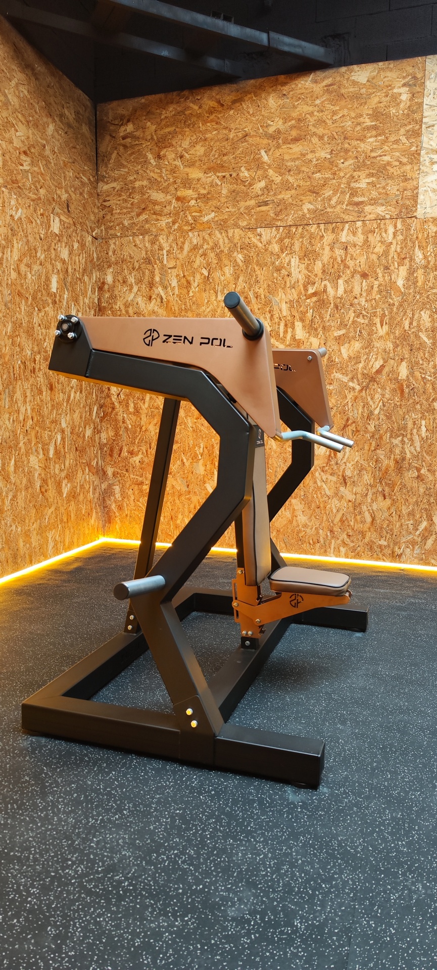 Equipamento de ginásio com assento castanho claro ZEN POL em ambiente com paredes de madeira e chão preto