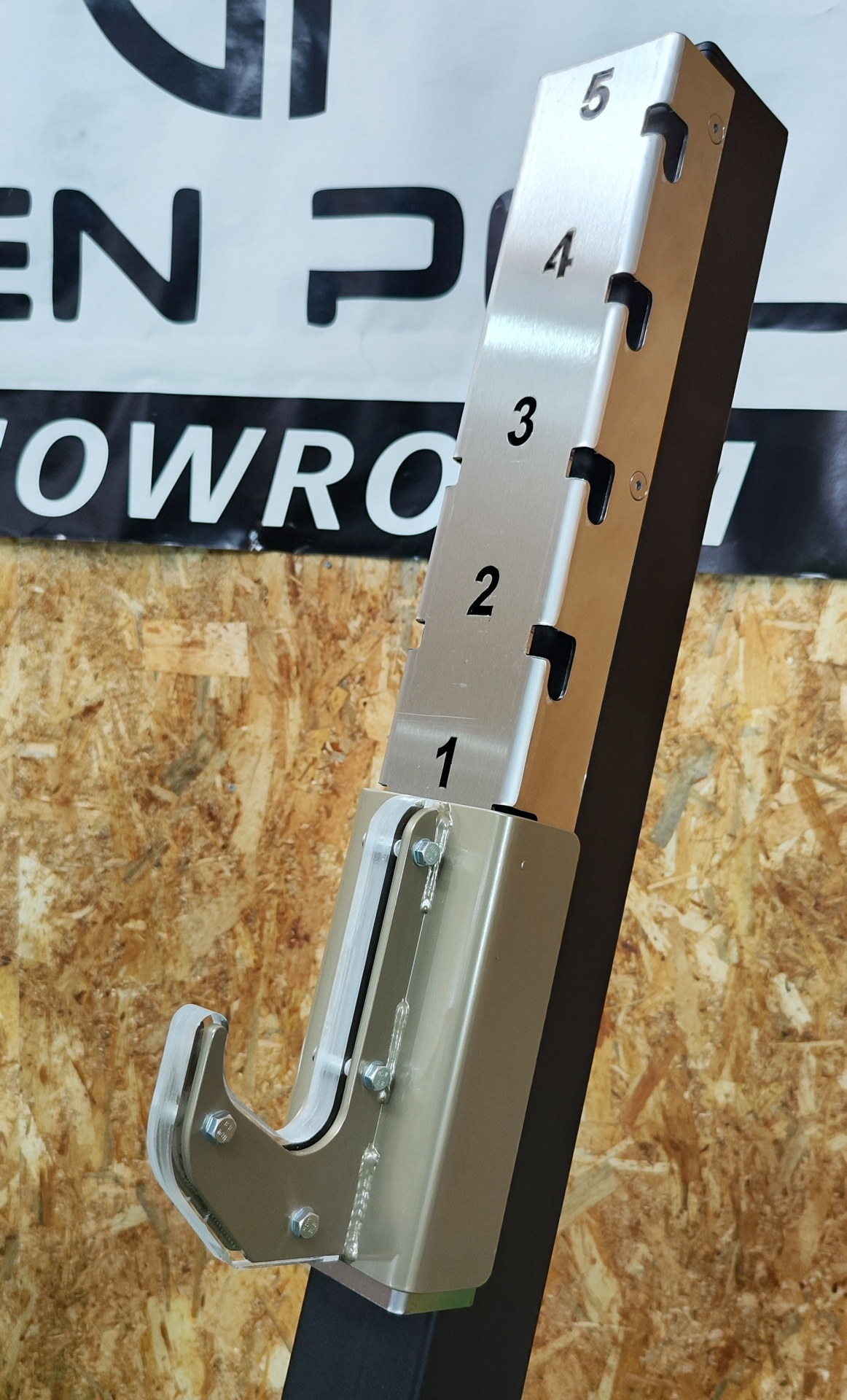 Suporte metálico com numeração e gancho contra parede de madeira com banner ao fundo