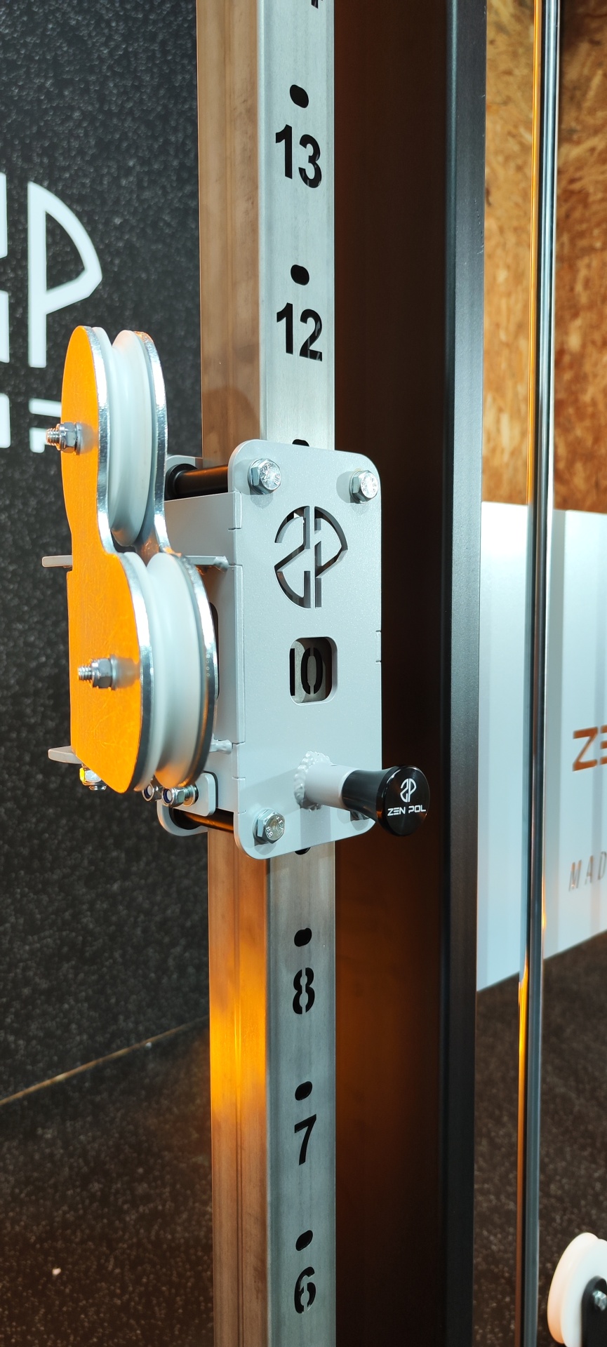 Equipamento de ginásio metálico com números e roletes laranja para cabos.