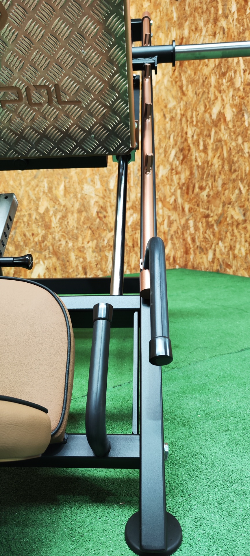 Máquina de treino de força com assento bege, estrutura preta e plataforma metálica antiderrapante.