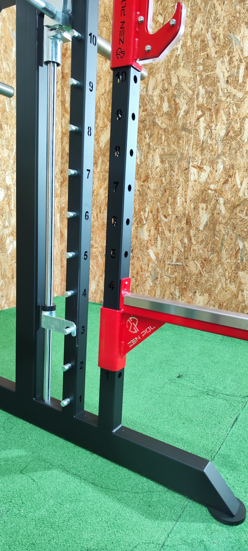 Estrutura metálica preta com detalhes vermelhos para exercício físico com numeração em fundo de parede de madeira e chão verde