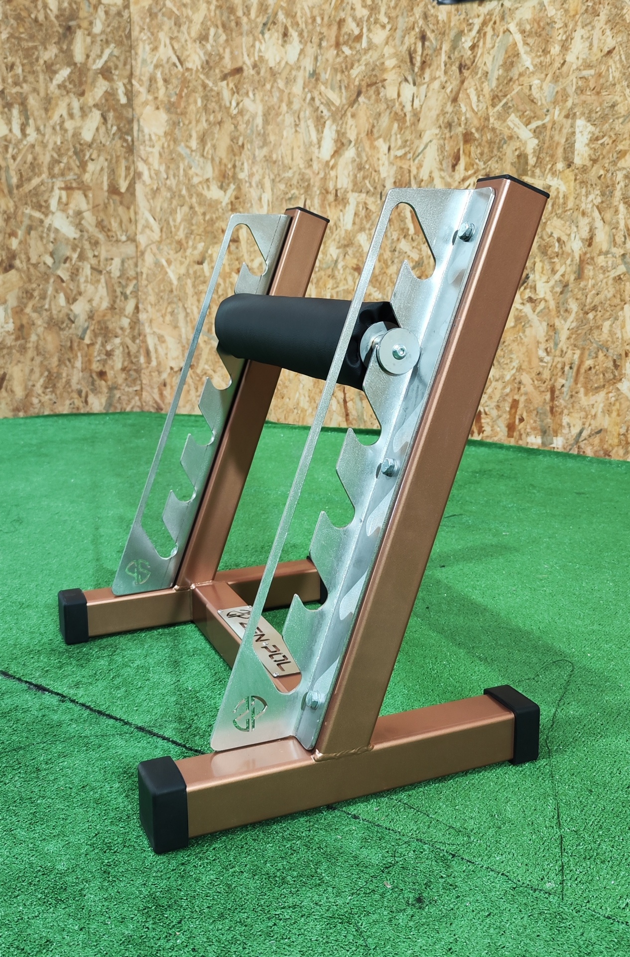 Suporte metálico para barra de exercício com acabamento cobre e base preta, sobre chão verde