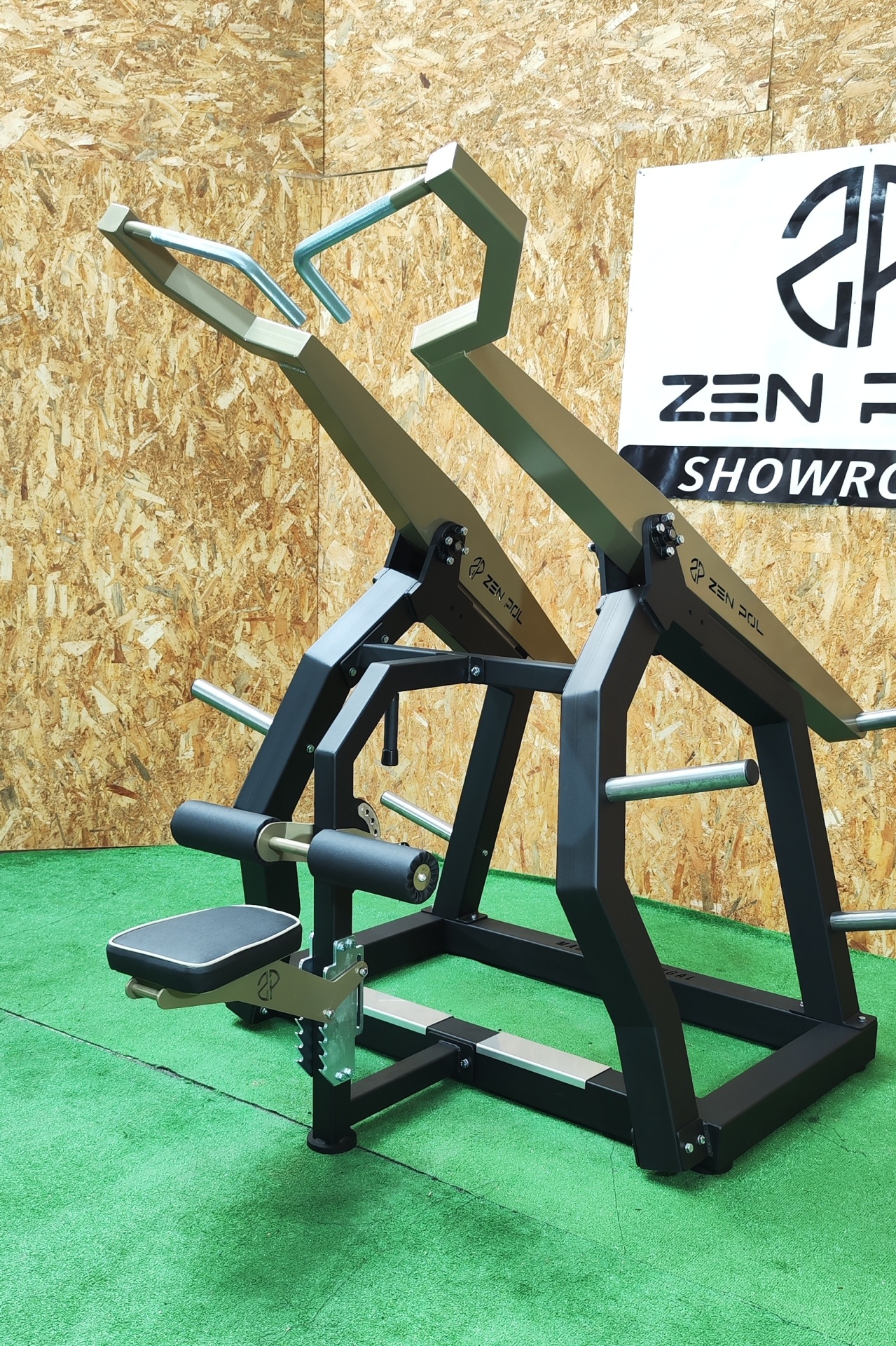 Equipamento de ginásio preto e cinza para treino de costas em ambiente interior com parede de madeira e tapete verde