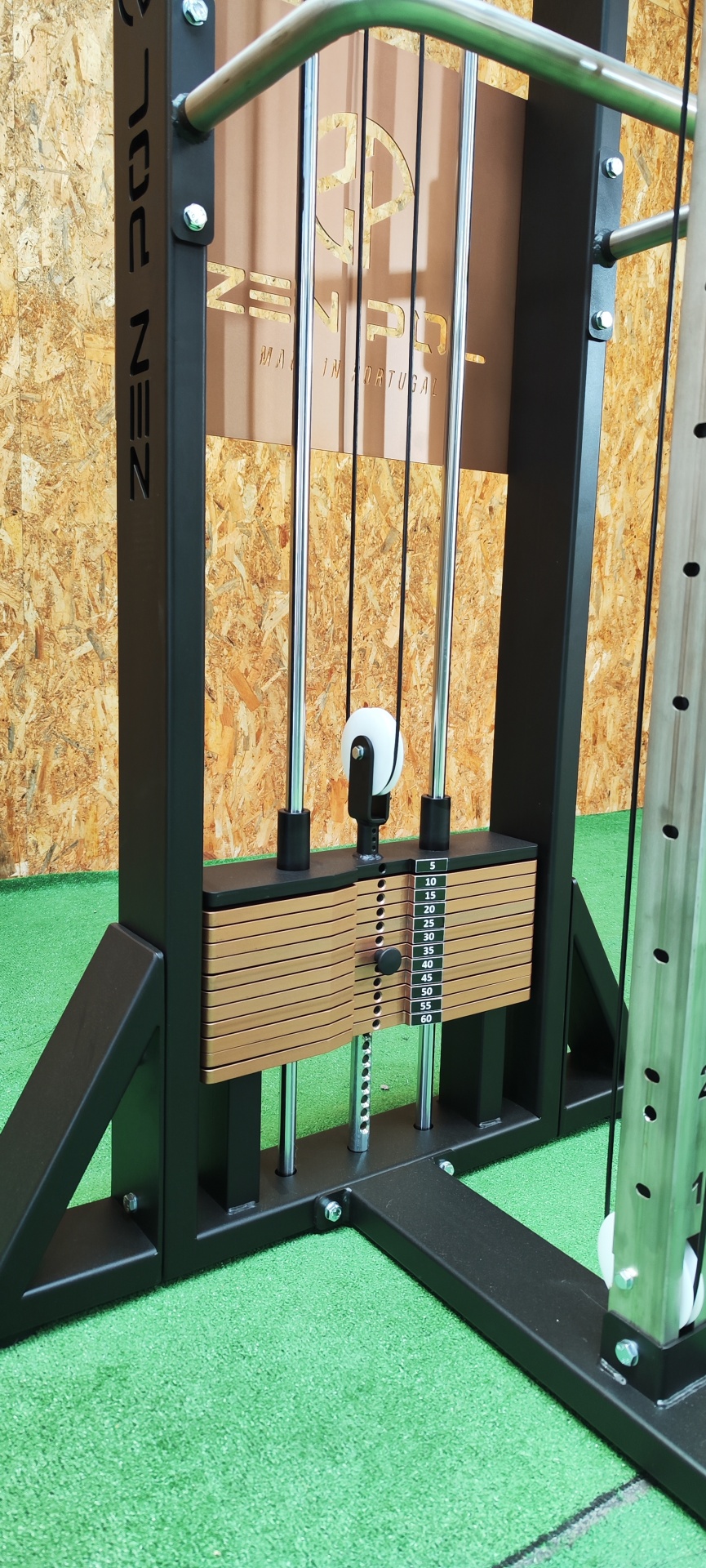 Máquina de musculação com placas de peso, estrutura preta e painel de madeira com logo Zen Pool.