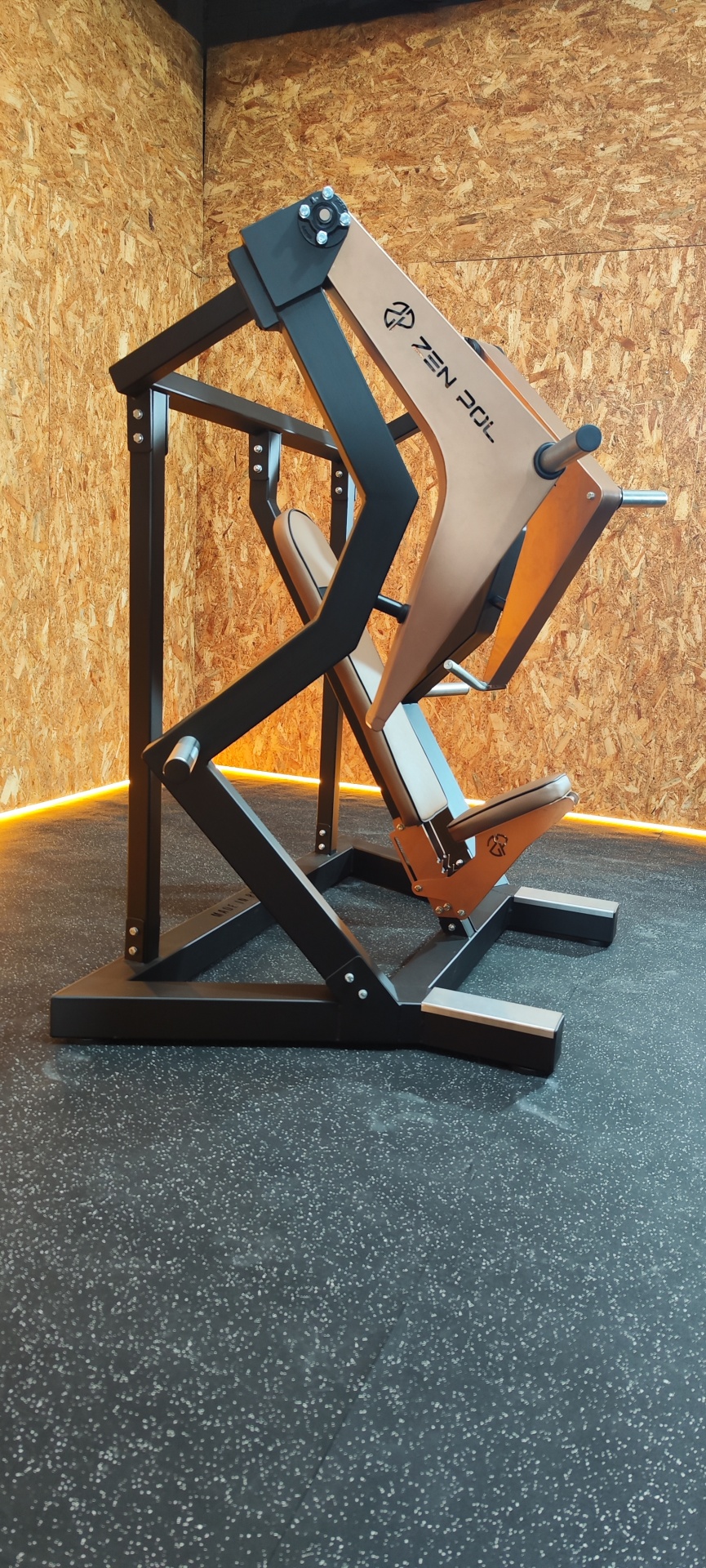 Máquina de exercício peitoral preta e bege com parede de madeira e chão preto