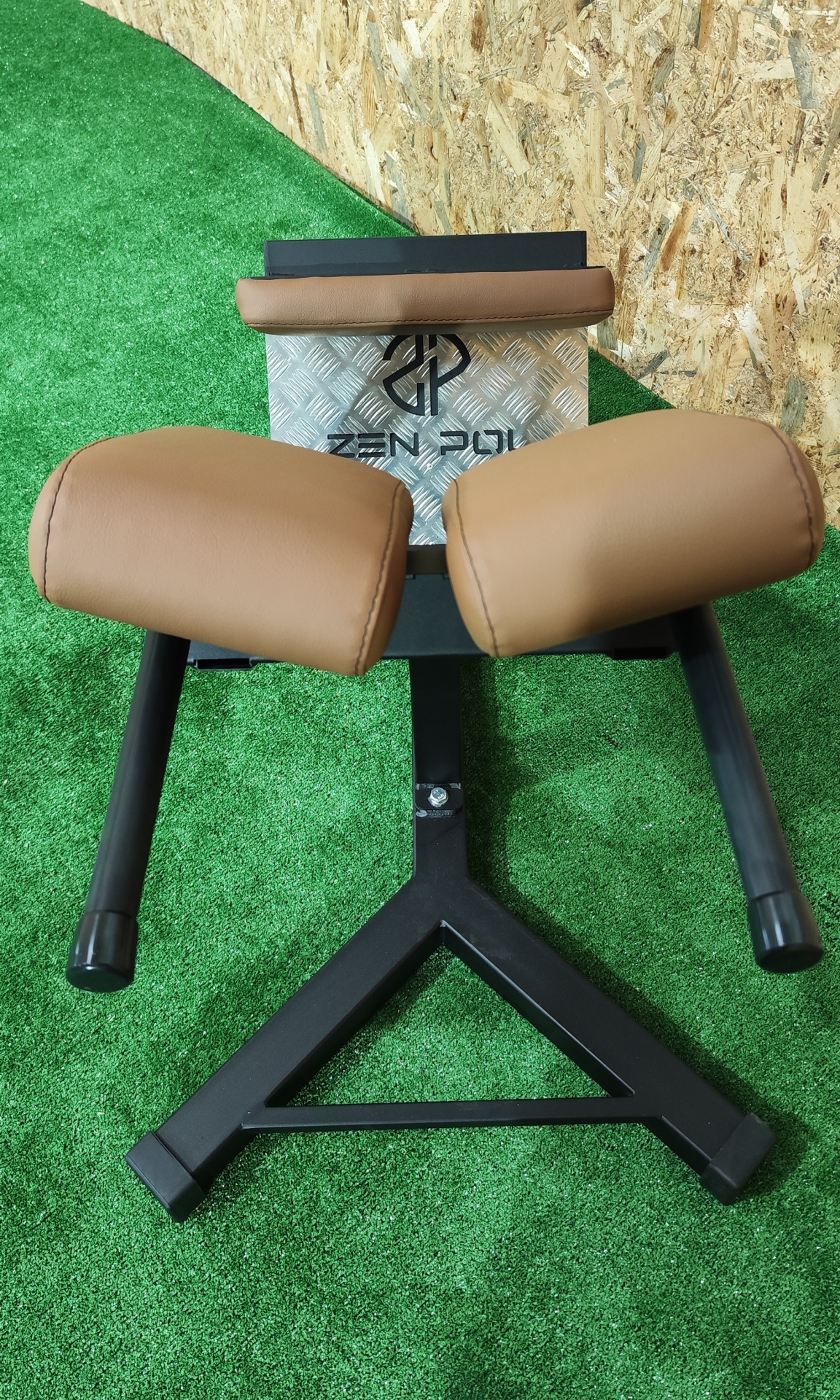 Equipamento de ginásio com estrutura preta e almofadas marrons em relva sintética e madeira