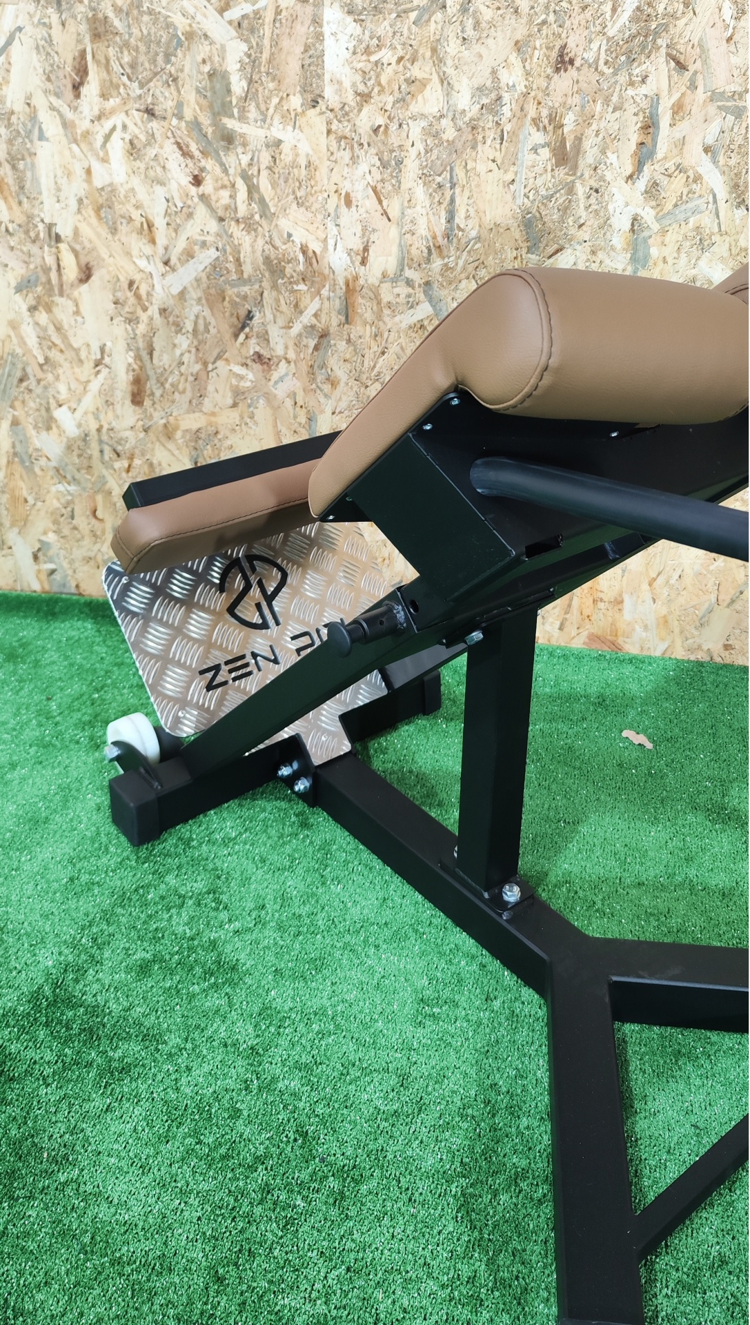 Banco de exercício com assento e encosto castanhos e estrutura metálica preta sobre relva artificial