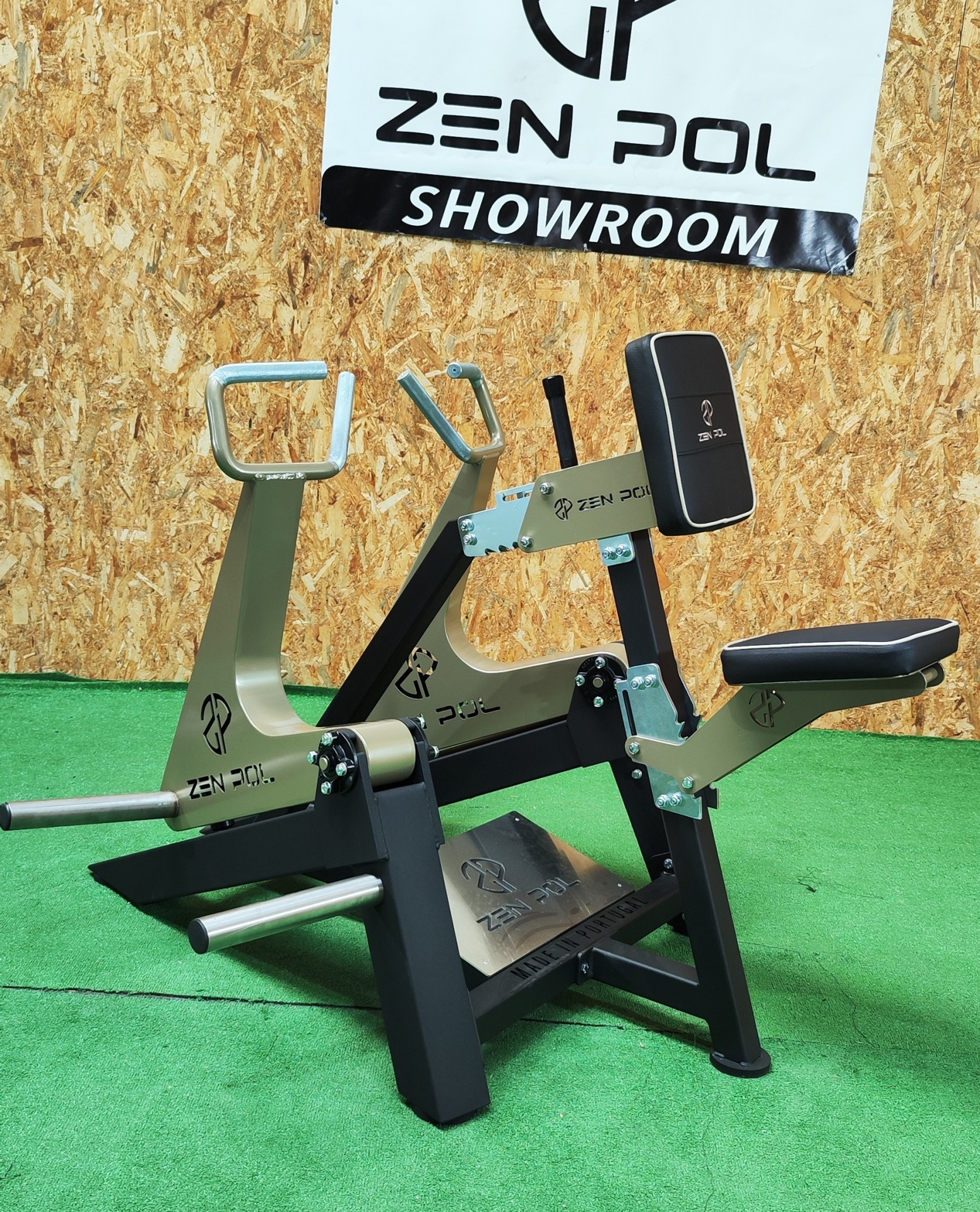 Máquina de treino de bíceps em ginásio, preta e dourada com assento preto e tapete verde.