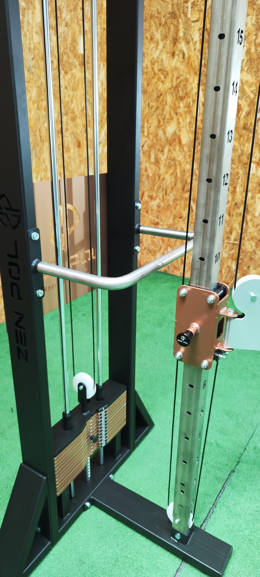 Aparelho de ginásio com pesos, cabos e barra metálica em fundo verde e madeira