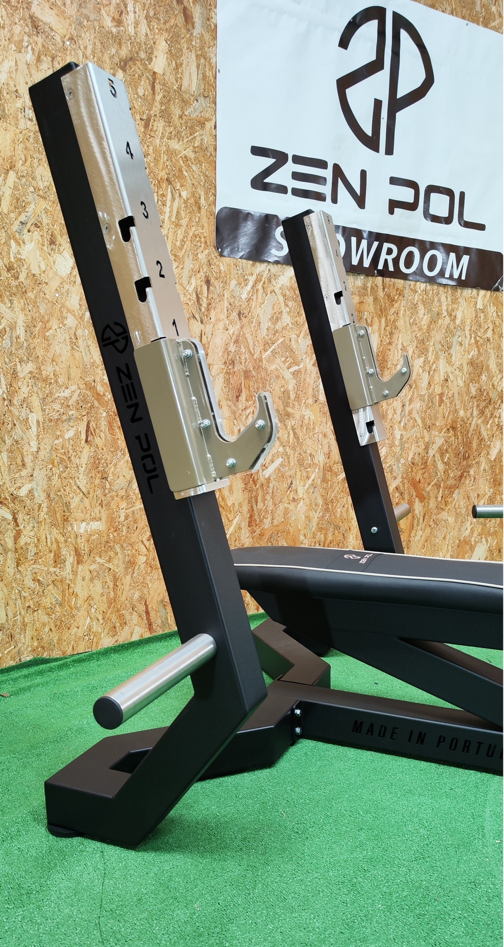Suporte de banco de musculação ZEN POL em metal preto e prateado com numeração, sobre piso verde sintético.